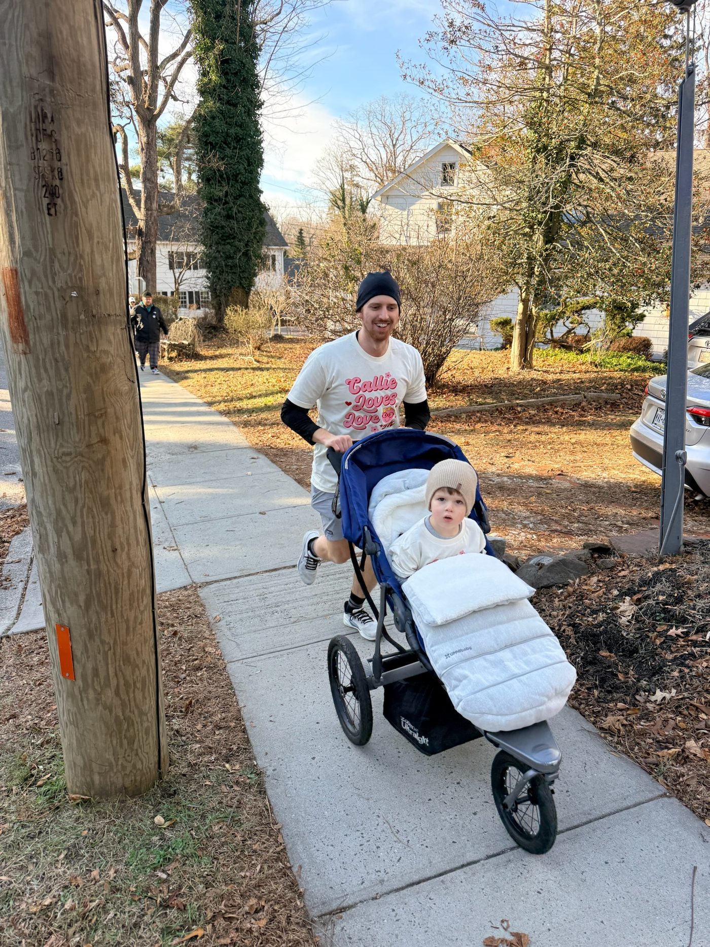 A runner in a race shirt pushing a toddler in a jogging stroller
