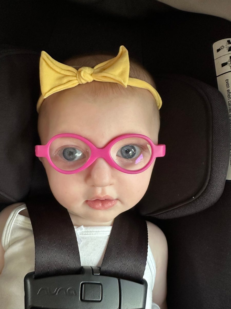 Callie in her car seat wearing pink glasses and a yellow bow